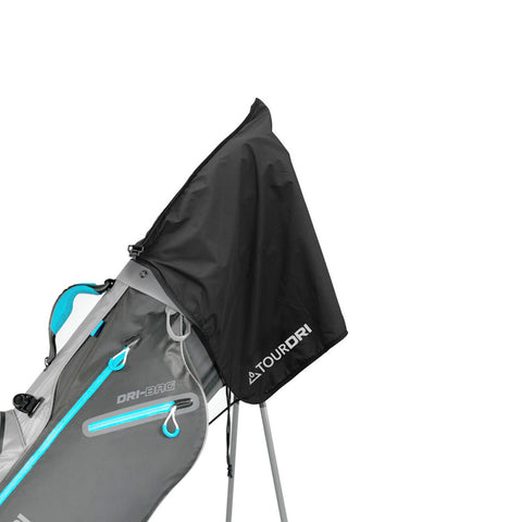 A golf bag with a grey body and turquoise accents stands upright with a black rain cover attached to its top in an indoor setting.