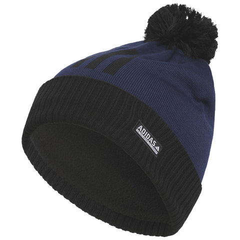 A blue knitted beanie with a black ribbed brim and a pompom on top is displayed at an angle showcasing its texture and design details including an Adidas logo on the trim.