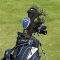 A golf bag stands on green grass holding various clubs with protective covers the bag is navy blue with white accents and has multiple pockets for accessories.