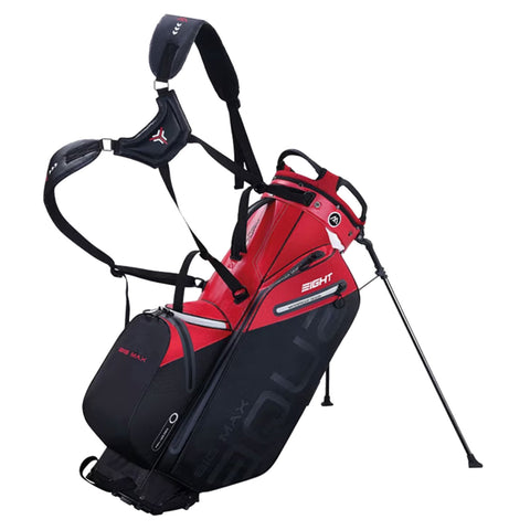 A red and black golf bag stands upright featuring a dual-strap system for carrying with a side pocket and a support leg extended, suitable for outdoor golfing environments.