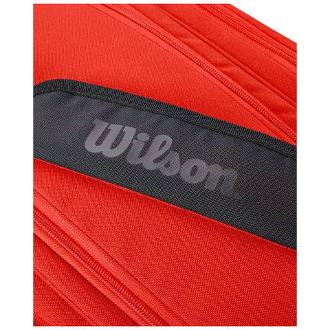 A vibrant red bag is shown with a prominent black strap featuring the brand name Wilson highlighted in gray the bag's zipper details are partially visible in the image