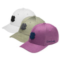 Three baseball caps are displayed in a row with distinct colors including white green and purple each featuring a clover emblem the purple cap has text that reads Live Lucky