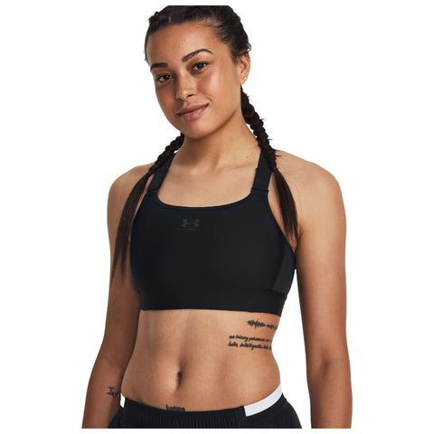 A young woman with braids is smiling while wearing a black athletic crop top and shorts showcasing her confident pose and fitness style against a plain background.