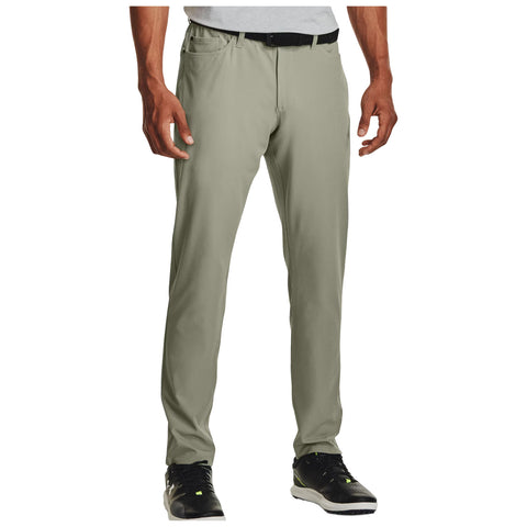 Light green pants are displayed standing upright with a relaxed fit while a person wears black athletic shoes. The upper portion shows a gray shirt and a black belt in a neutral setting.