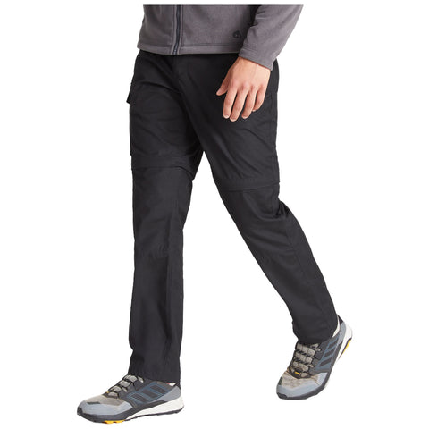 A person wearing black hiking pants and gray hiking shoes is walking forward, their right foot lifted while the left remains flat on the ground, set against a neutral background.