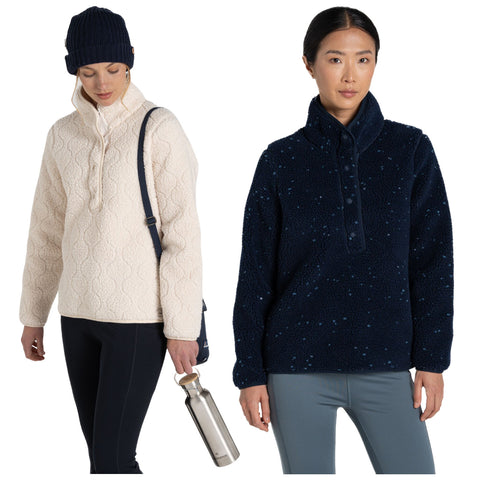 Two women stand side by side wearing cozy, stylish outerwear. The woman on the left wears a light-colored pullover and holds a water bottle, while the woman on the right dons a dark pullover.