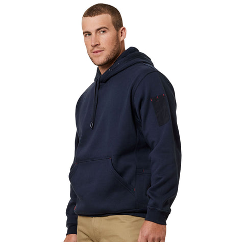 A man is wearing a navy blue hooded sweatshirt with a front pocket and red stitching while standing in a neutral environment, gazing slightly to the side.