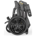 A compact, foldable wheelchair stands upright with its large black wheels prominently displayed and various mechanical components visible, set against a plain white background.