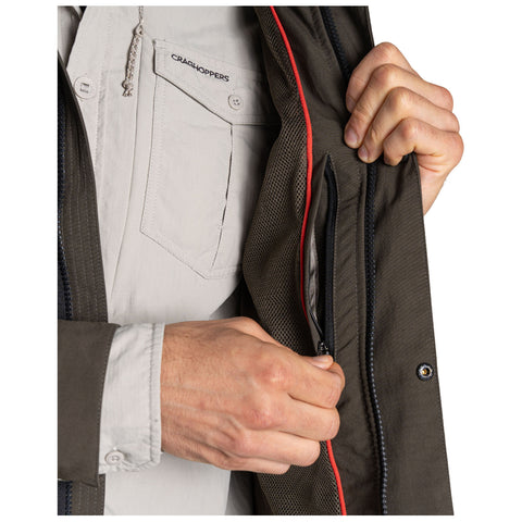 A hand reaches for a zippered pocket on the inside of a brown jacket revealing a contrasting interior fabric with a mesh texture amidst a neutral background.