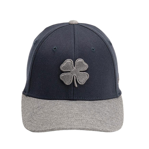 A dark baseball cap features a stitched gray four-leaf clover emblem on the front and a matching gray visor at the bottom with a textured finish outlining the cap's structure.