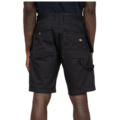 Black cargo shorts with multiple pockets are worn by a person standing with their back facing the viewer in a neutral or light background possibly indicating a casual or work environment.