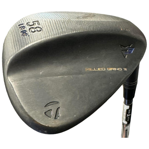 A golf wedge lies on a flat surface showcasing its curved face and textured surface with markings indicating 58 degrees and the text Milled Grind 3 near the sole and brand logo.