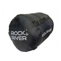 A black cylindrical bag is lying on a white background featuring the text ROCK+RIVER in large white letters and a strap is attached on the side for securing it.