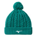 A teal knit beanie with a pom-pom on top is displayed upright showcasing textured cable stitching and a ribbed cuff featuring a white logo on the front.