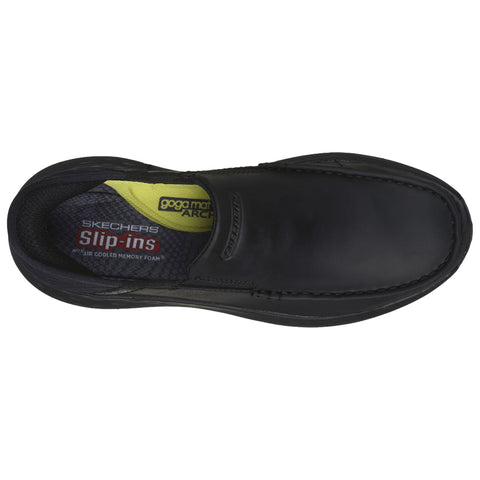 A black slip-on shoe is displayed with a cushioned insole labeled goga mat arch and air cooled memory foam resting on a flat surface highlighting its sleek design and comfort features.