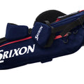 A navy blue golf bag features a red accent and a logo on the side. It has compartments for clubs and an adjustable strap for carrying in a golfing environment.