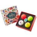 A colorful birthday-themed box contains five golf balls with various designs including the text "Happy Birthday". The setting is festive, suggesting a gift for a golf enthusiast's birthday celebration.