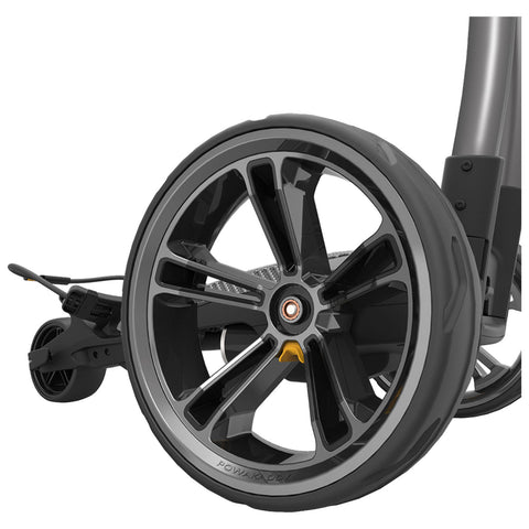 A black and silver wheelchair wheel is positioned prominently with a sleek design showcasing multiple spokes while attached to a frame suggesting mobility in an indoor space.