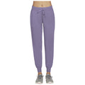 Purple sweatpants are being worn by someone standing in a neutral space with gray athletic shoes on their feet showcasing a comfortable and casual athletic look. The drawstring waist is visible.