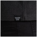 A dark textured fabric features a visible clothing label while being worn above black pants in a neutral setting emphasizing the outdoor brand Craghoppers which promotes authentic outdoor wear since 1965.