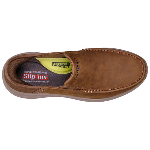 A brown slip-on shoe rests facing upward showcasing its smooth leather exterior and cushioned insole with "SKECHERS" branding and "Air Cooled Memory Foam" label visible inside.