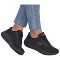 Black sneakers are worn on feet positioned together with jeans that have frayed cuffs The sneakers feature a mesh design and a textured sole suitable for casual wear or exercise