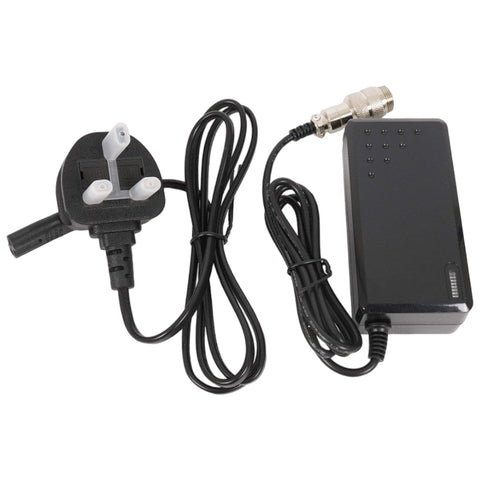 A black power adapter with an attached three-pin plug on one side and multiple cables extending from it connects to an electronic device in a typical home or office setting.