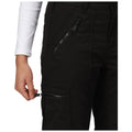 A hand grips the zipper of a black cargo pant's pocket while wearing a long-sleeve white shirt in a neutral setting, indicating the action of opening or closing the pocket.