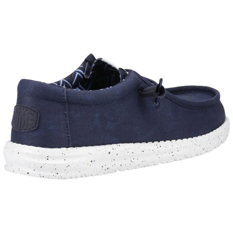 A navy shoe with a white speckled sole is positioned at an angle showing its rounded design and shoelace detail aimed for casual wear in a relaxed setting.