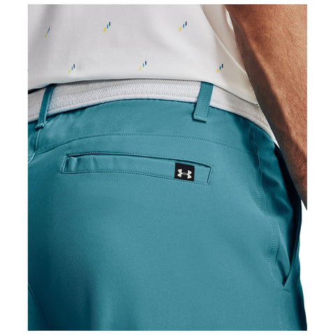 Teal shorts are worn by a person whose upper part is partially visible featuring a white shirt with a pattern while showing the back pocket and logo of the clothing brand in a casual setting.