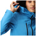 A person is adjusting the collar of a bright blue jacket with a zippered pocket in a close-up view, showcasing the garment's design and fit against a plain background.