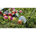 A golf club is poised to strike a brightly colored golf ball sitting on lush green grass among a cluster of similar colorful balls in the background.