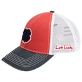 A baseball cap showcases a vibrant red fabric front with a black and white four-leaf clover design and a gray brim featuring the phrase Live Lucky in red on the side.