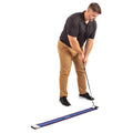 A man in a black polo shirt and tan pants is preparing to putt a golf ball on a training mat designed for alignment and practice, focusing intently on his shot.