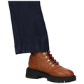 A brown lace-up boot with red laces is positioned below a dark navy pant leg in a neutral setting emphasizing the footwear's details and rugged design.