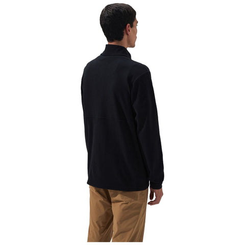 A man wearing a black fleece pullover stands with his back to the viewer in a neutral setting with a white background, indicating a casual or outdoor attire.