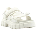 White sandals feature thick straps and a chunky sole. They rest on a flat surface, showcasing a modern, casual design suitable for warm weather or relaxed settings.