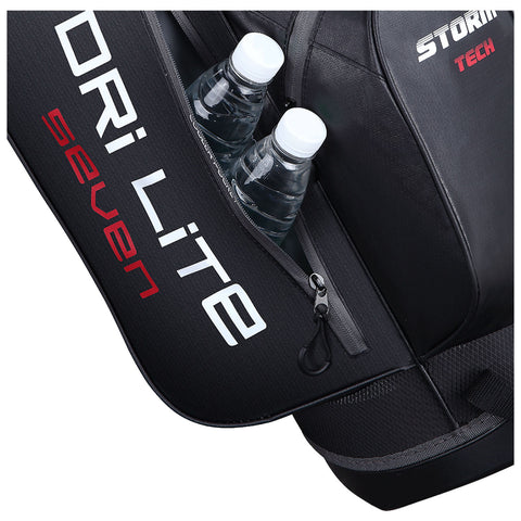 A black backpack with a zipper compartment holds two clear water bottles with white caps visible from the opening featuring branding that reads DRILITE SEVEN and STORM TECH.