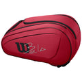 A red tennis bag features the Wilson logo and a signature. It is designed with two compartments and a sleek shape, suggesting it is intended for carrying sports equipment.