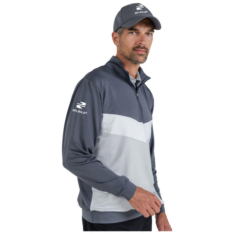 A man wearing a gray and white golf jacket and a matching cap stands confidently. He gestures with one hand while facing the viewer against a plain white background.