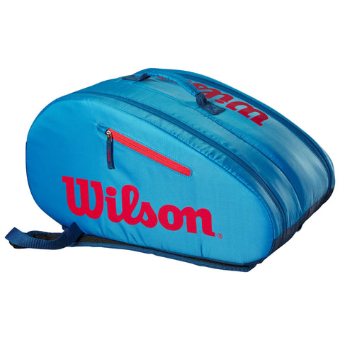 A blue tennis bag with red zipper and logo houses sports equipment and is placed on a flat surface with no visible background elements.