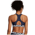 A navy blue sports bra with a racerback design is being worn by a person facing away, revealing the fabric's texture and the prominent logo on the elastic band.