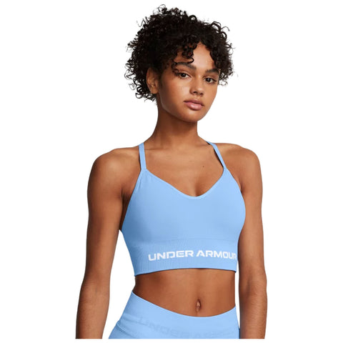 A young person with curly hair is wearing a light blue sports bra featuring the brand name UNDER ARMOUR prominently displayed in white at the bottom, posing against a plain background.