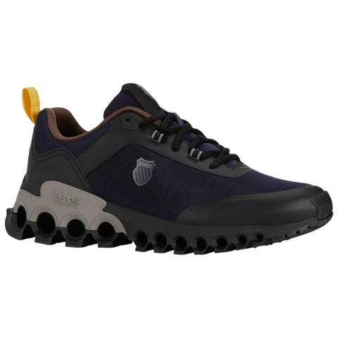 A sneaker with a dark blue upper and black rubber sole featuring circular cutouts sits quietly showcasing a modern design and a small yellow pull tab at the heel