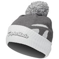 A gray and white knit beanie with a pom-pom on top features the logo "TaylorMade" prominently on the front, designed for warmth in cold weather environments.