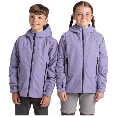 Two children stand side by side wearing matching light purple jackets with hoods smiling at the viewer their hands are relaxed at their sides and they are in a neutral background