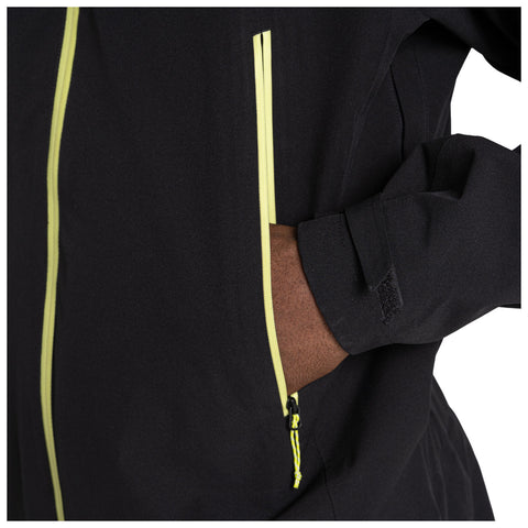 A black jacket with yellow zippers is displayed the jacket's pocket is slightly open revealing a hand placed inside the pocket the fabric appears smooth and fitted