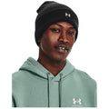 A young man is wearing a black beanie and a light green hoodie with a logo. He is looking directly at the viewer with a neutral expression.