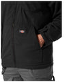 A black jacket is being worn by a person with one hand placed inside a pocket while the other hand rests at the side with the fabric appearing sturdy and casual