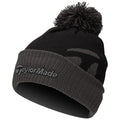 A black knit beanie with a pom pom on top features a folded cuff displaying the TaylorMade logo in gray against the black fabric, suitable for cold weather wear.